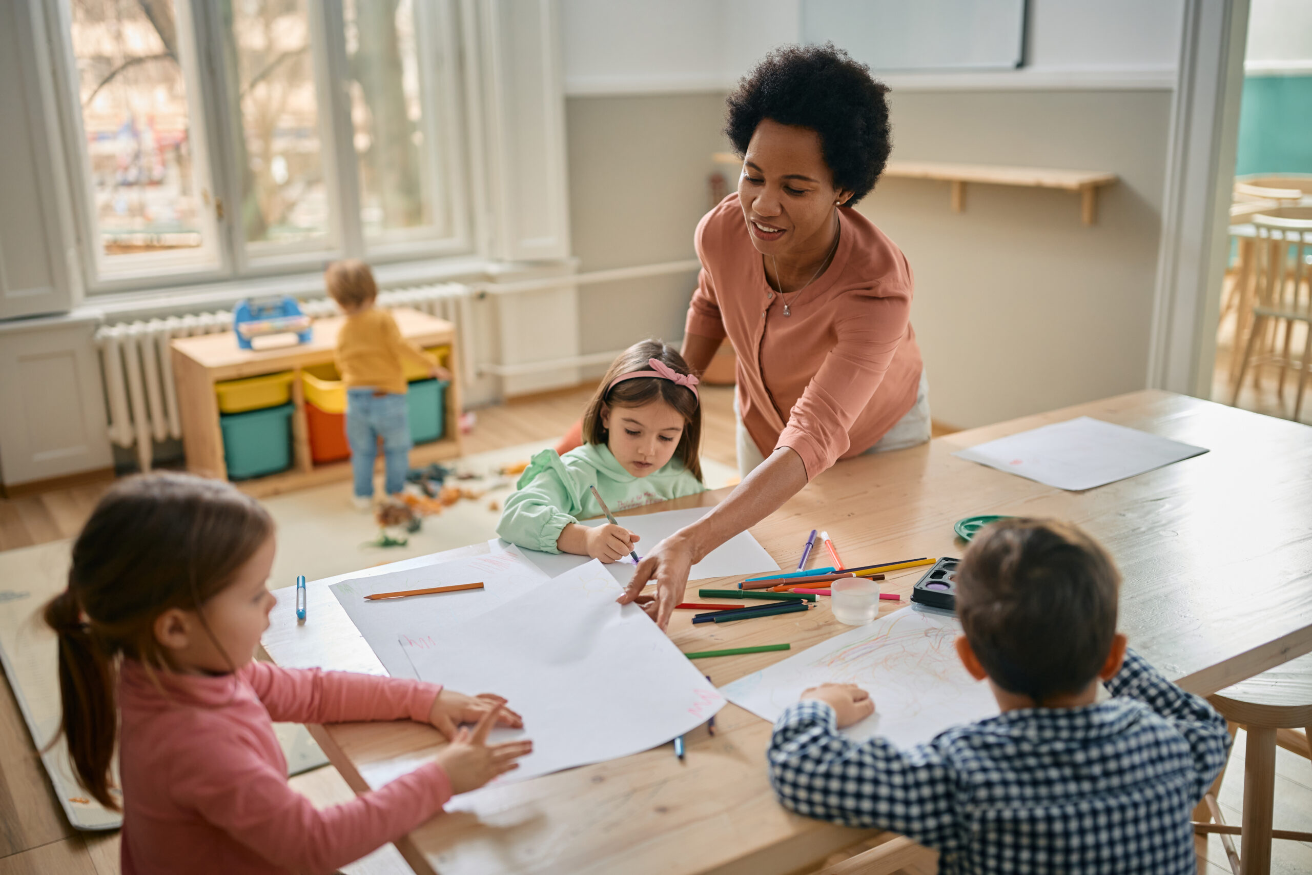 Woman helping children to color at a table.